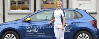 Ambulante Pflege Daheim Pflegerin steht vor einem blauen Kleinwagen mit der Aufschrift: "St. Marien - Ambulante Pflege Daheim - Deutscher Orden"